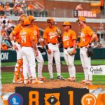 Tennessee Volunteers players in orange uniforms huddle on the pitcher’s mound during a game; scoreboard shows 8–1 with team logos.