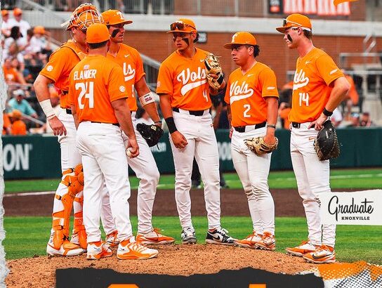 Tennessee Volunteers players in orange uniforms huddle on the pitcher’s mound during a game; scoreboard shows 8–1 with team logos.