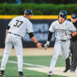Two baseball players in white pinstriped uniforms high-five on the bases during a game, one wearing number 37 and the other with a WF helmet.