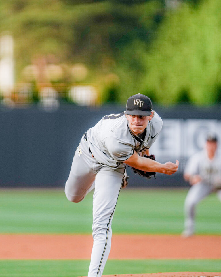 Baseball pitcher in gray uniform delivering a pitch on a mound, WF cap visible, field blurred in background