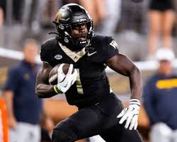 African American football player in a black uniform running with the ball on a football field.