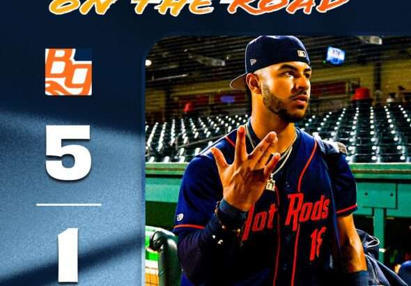 Baseball player in a blue jersey and cap walks out from the dugout on a promotional poster that reads 'WIN ON THE ROAD' at the top.