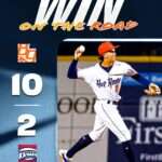 Poster-style image of a baseball pitcher in a white Hot Rods uniform throwing a pitch, with 'WIN ON THE ROAD' title and a vertical 10–2 score on the left.