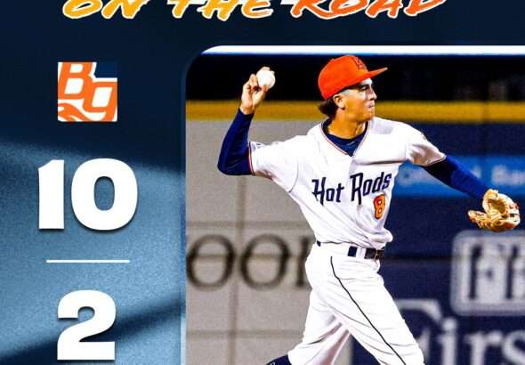 Poster-style image of a baseball pitcher in a white Hot Rods uniform throwing a pitch, with 'WIN ON THE ROAD' title and a vertical 10–2 score on the left.