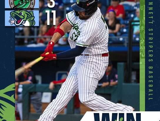 Baseball player in a white pinstripe uniform swings at a pitch on the field; scoreboard shows 3–11 with team logos and a bold 'WIN' graphic, Northside Hospital logo visible.