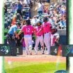 Baseball players in pink uniforms celebrate on the field after a 4–1 victory; final score displays 1–4 with team logos visible.
