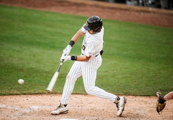 Baseball player in striped uniform swings at a pitched ball near home plate on a green field.