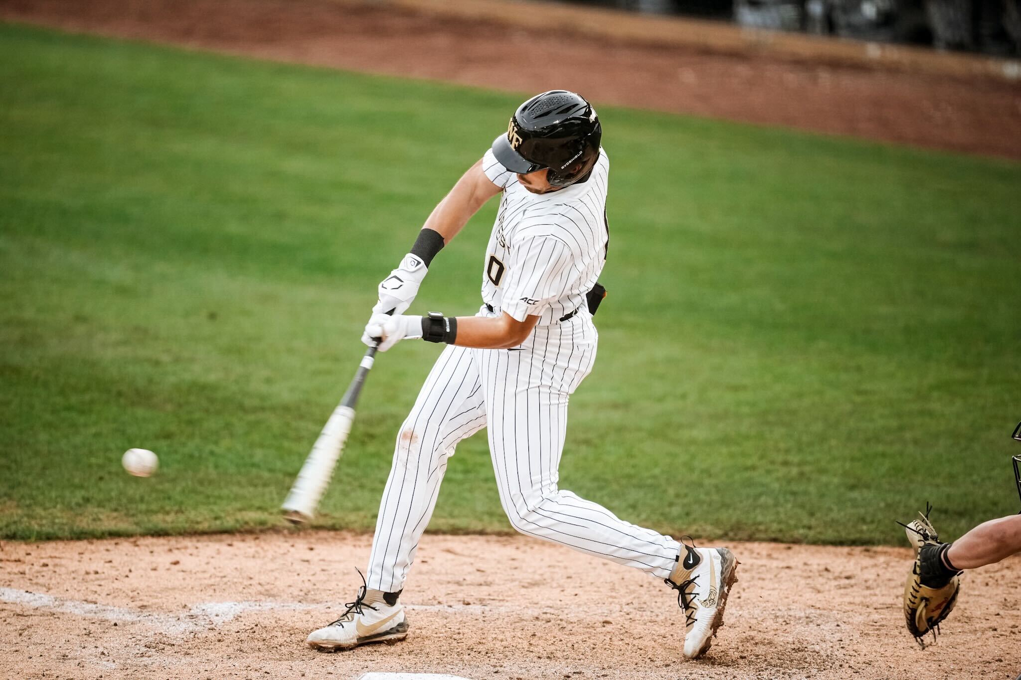 Baseball player in striped uniform swings at a pitched ball near home plate on a green field.
