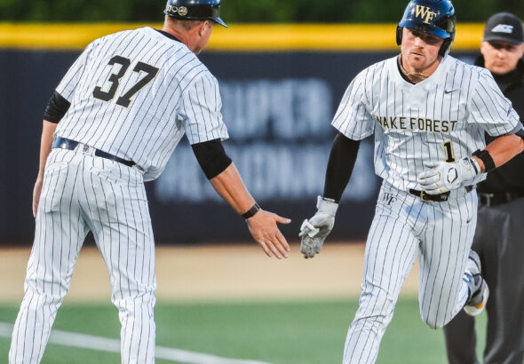 Two Wake Forest baseball players in white pinstripe uniforms celebrate on the infield, one with the number 37 on his back.