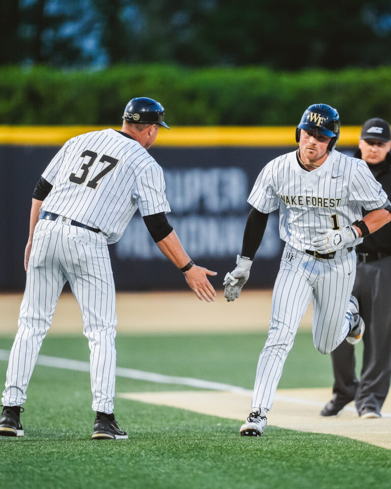 Two Wake Forest baseball players in white pinstripe uniforms celebrate on the infield, one with the number 37 on his back.
