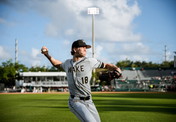 Baseball pitcher in mid-pitch on a sunny field wearing a WAKE uniform, ball in hand ready to throw.