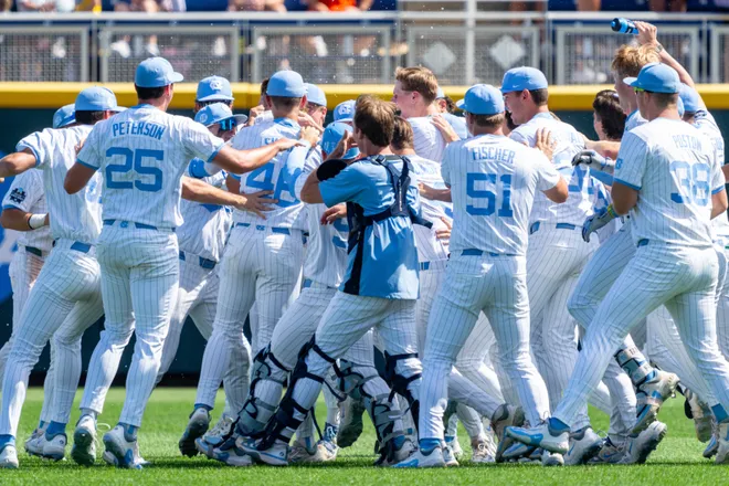 Baseball team in white uniforms huddling and celebrating on the field.