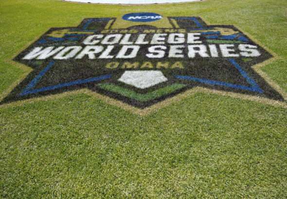 » Greenville Sports Media College World Series logo painted in turf on a baseball field, with green grass surrounding it.