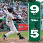 Batter in a white baseball uniform swings at a pitch in the batter's box with crowds in the stands; a tall green final banner stands to the right with a large 9 and 5 and the date June 11, 2026.