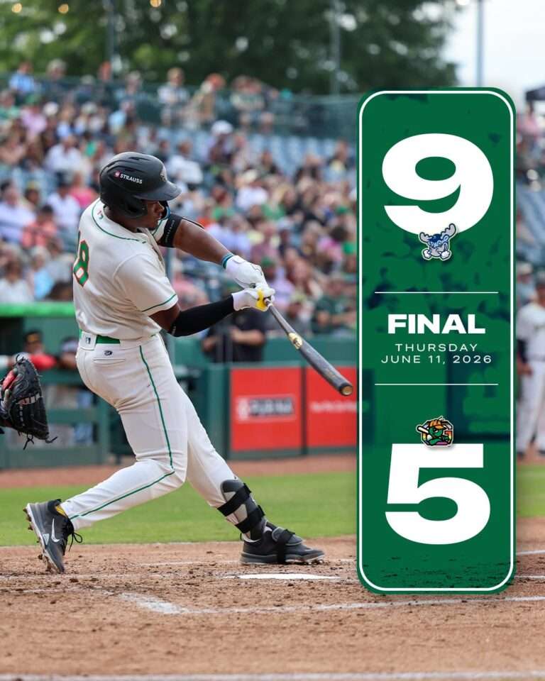 Batter in a white baseball uniform swings at a pitch in the batter's box with crowds in the stands; a tall green final banner stands to the right with a large 9 and 5 and the date June 11, 2026.