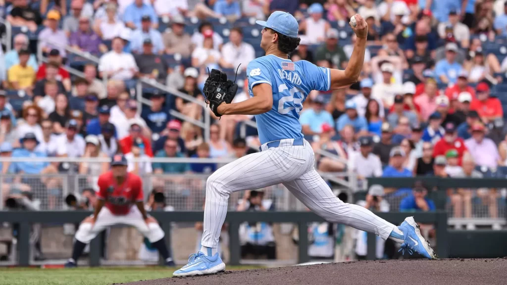 resize 5 » Greenville Sports Media Baseball pitcher in a light blue uniform throwing a pitch on the mound with a crowded stadium in the background.