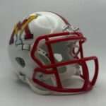 White American football helmet with a red facemask and a colorful NY-style logo on the side by the shell edge.