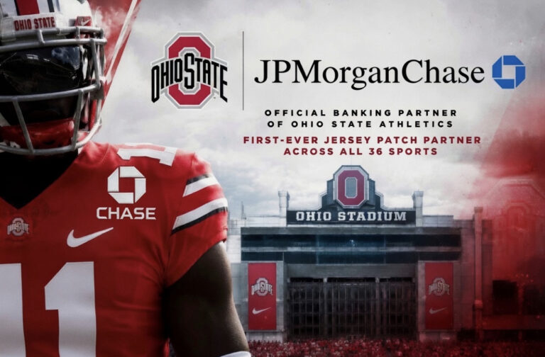 Ohio State football player in red jersey with sponsor logos, standing before Ohio Stadium banner.