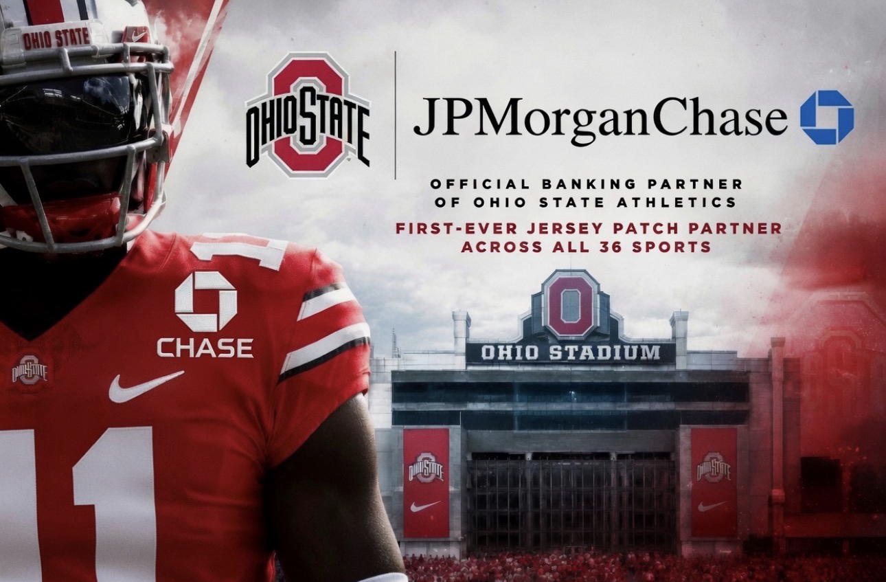 Ohio State football player in red jersey with sponsor logos, standing before Ohio Stadium banner.