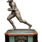 Bronze statue of a football player running, mounted on a wooden base with a plaque.