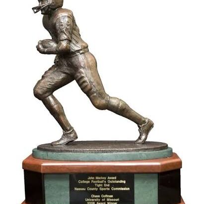 Bronze statue of a football player running, mounted on a wooden base with a plaque.